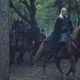 King Viserys rides on a brown horse through the forest, his massive retinue trailing behind him.